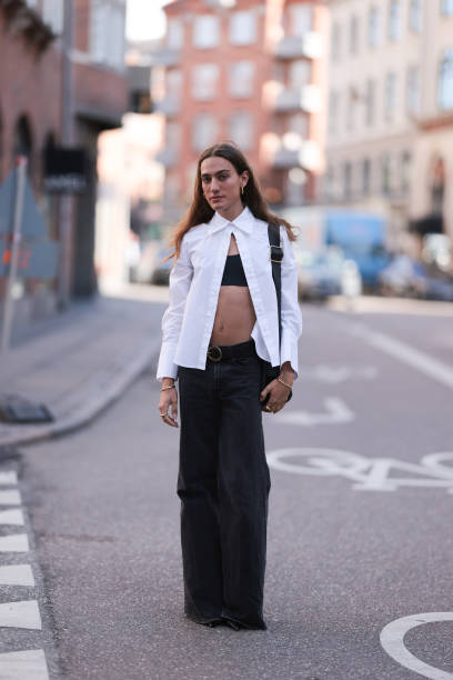 George Gorg is seen wearing golden hoop earrings; a white, long-sleeved shirt with a wide collar that is only buttoned at the top; underneath a black...