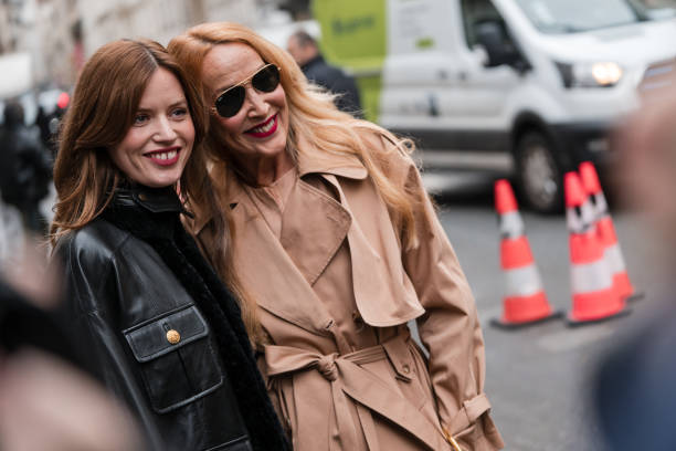 Georgia May Jagger wears black leather jacket with fur details, beige Chloe bag, and Jerry Hall wears beige trench coat, outside Chloe, during the...