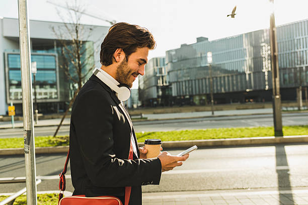 germany, frankfurt, young businessman walking the city with cup of coffee, using mobile phone - junk food stock pictures, royalty-free photos & images
