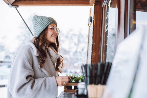 get warm with street coffee or tea. smiling woman in warm clothes hold credit card, treating herself near food and drink stall in winter streets - junk food stock pictures, royalty-free photos & images