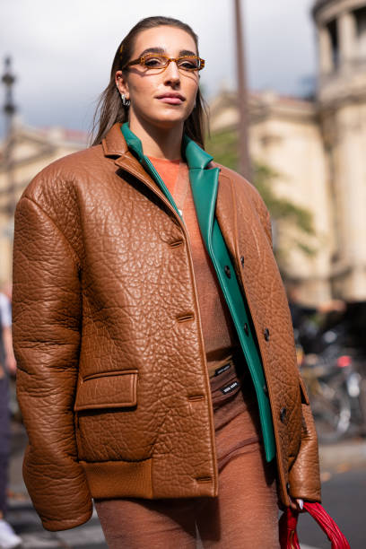 Ginevra Mavilla wears nude cardigan, green leather blazer, brown leather jacket and brown sheer skirt, outside Miu Miu, during the Womenswear...