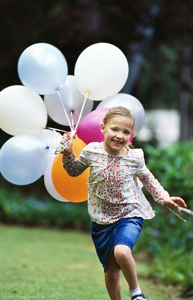 girl (8-9) running with a bunch of balloons - garden decoration stockfoto's en -beelden