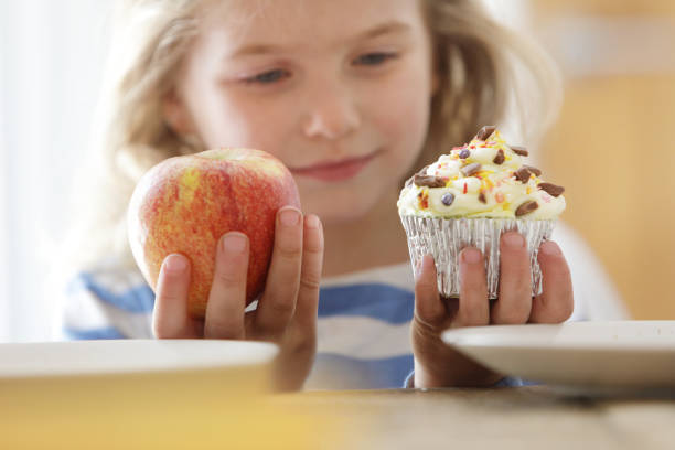 girl choosing between an apple and a cake - junk food stock pictures, royalty-free photos & images