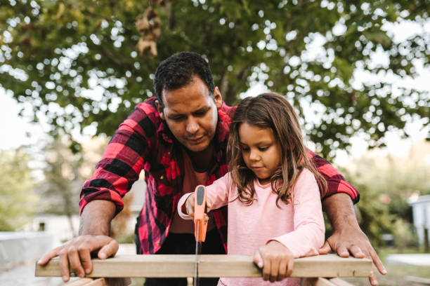 girl cutting wooden plank by father during summer - home decoration stock pictures, royalty-free photos & images