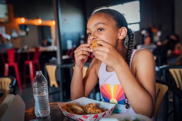 girl eating take out fried chicken with her fingers - junk food stock pictures, royalty-free photos & images