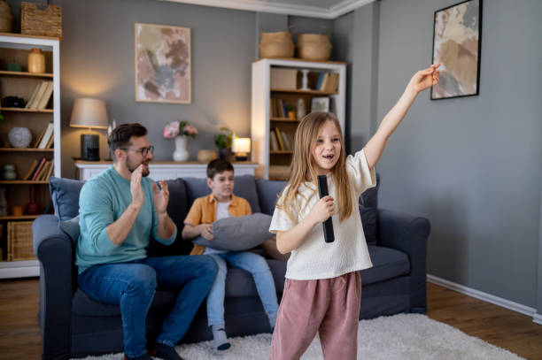 girl holding the remote controller as a microphone and performing at home - concert stock pictures, royalty-free photos & images