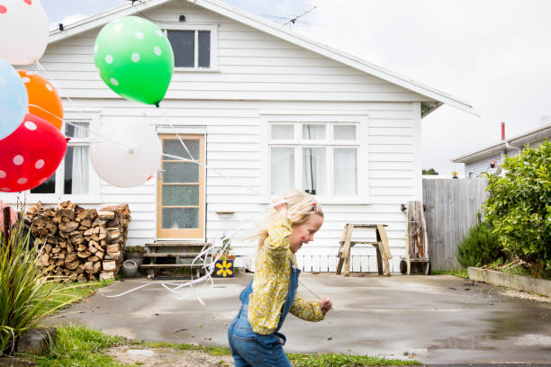 girl runs past the front of a bungalow holding colourful balloons - garden decoration stock pictures, royalty-free photos & images