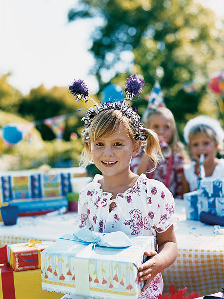 girl sitting holding a wrapped present at a birthday party - garden decoration stockfoto's en -beelden