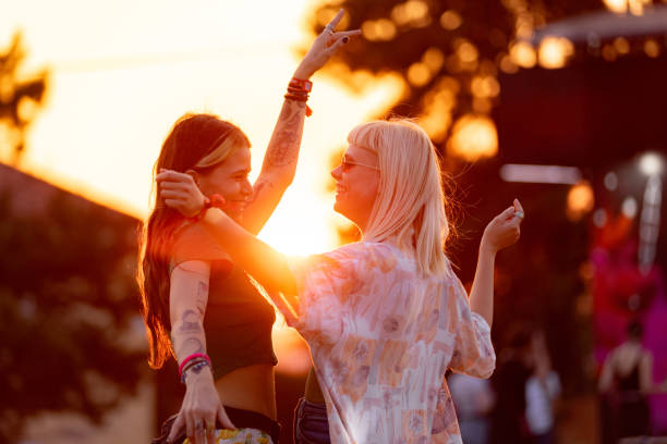 glückliche freundinnen, die sich während eines musikfestivals bei sonnenuntergang amüsieren. - concert stock-fotos und bilder