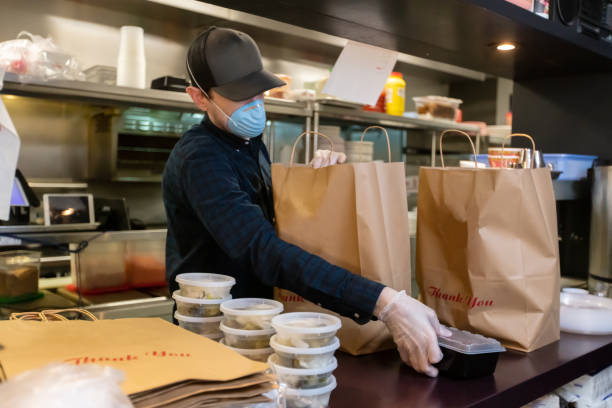 gloved and masked man in restaurant kitchen preparing food for delivery during covid-19 pandemic - junk food stock pictures, royalty-free photos & images