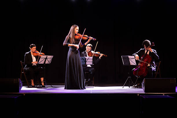 graceful violinist in a black, elegant dress playing the violin while standing in front of the rest of the string quartet - concert stock pictures, royalty-free photos & images