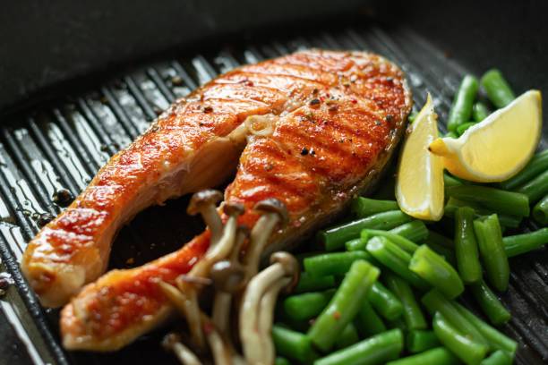 grilled salmon steak, baked piece of trout with green beans, shimeji mushrooms and lemon in a grilled pan. - junk food stock pictures, royalty-free photos & images