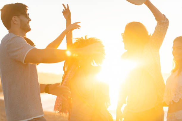 group of friends dancing and celebrating on the beach at sunrise/sunset. - concert stock pictures, royalty-free photos & images