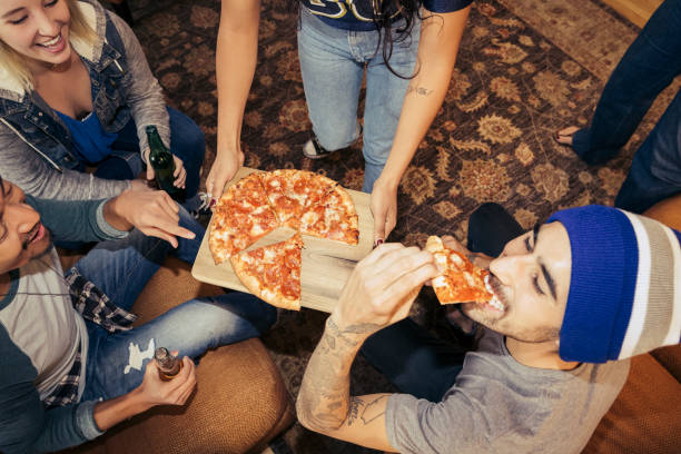 group of friends eating pizza and drinking beer at party - junk food stock pictures, royalty-free photos & images