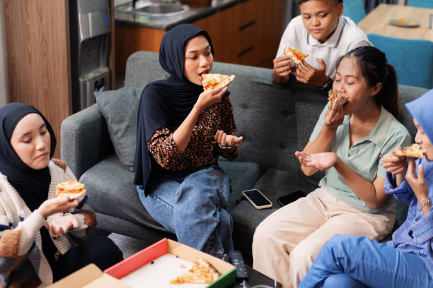 group of friends enjoying pizza together in casual indoor setting - junk food stock pictures, royalty-free photos & images