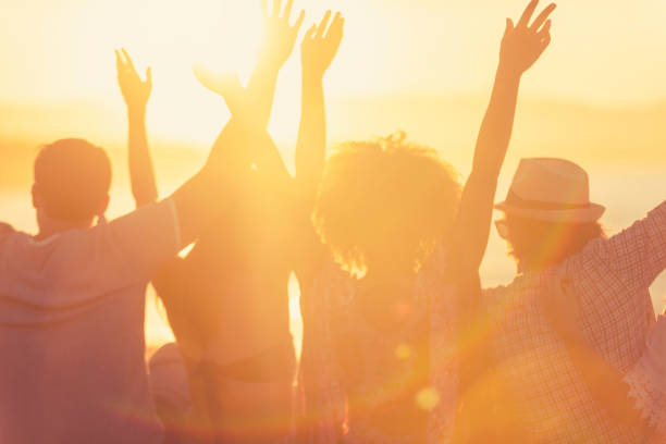 group of friends sitting on the beach at sunset/sunrise. - concert stock pictures, royalty-free photos & images