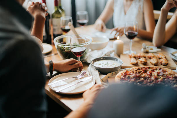 group of joyful young asian man and woman having fun, enjoying food and wine across table during party - food stock pictures, royalty-free photos & images