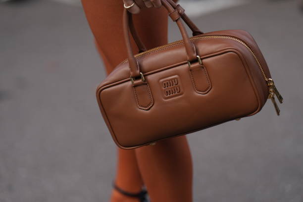 Guest holds a brown leather rectangle shaped bag from Miu Miu , outside Miu Miu, during the Womenswear Spring/Summer 2024 as part of Paris Fashion...