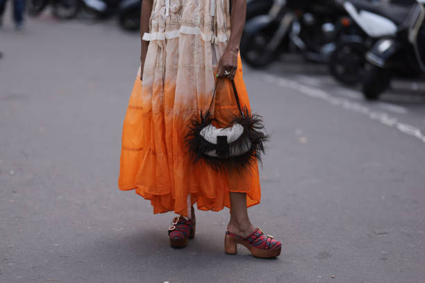 Guest is seen outside Zimmermann show wearing lilac Oakley sunnies, silver chain, white and orange ombre colored dress, beige hairy Fendi Baguette...