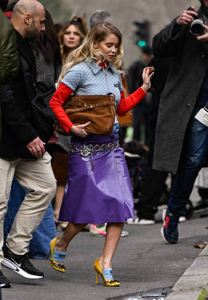 Guest is seen wearing a blue and red Miu Miu shirt, purple skirt, chain belt, brown bag and yellow and black heels with light blue Miu Miu socks...