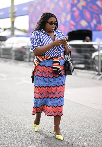 Guest is seen wearing a blue and white stripe shirt, red and blue skirt and lime green shoes with black sunglasses and a black bag outside the Dior...