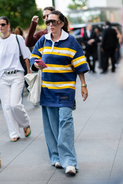 Guest is seen wearing a blue and yellow top, blue denim pant, white sneakers, brown sunglasses and carrying a white bag outside the Michael Kors show...