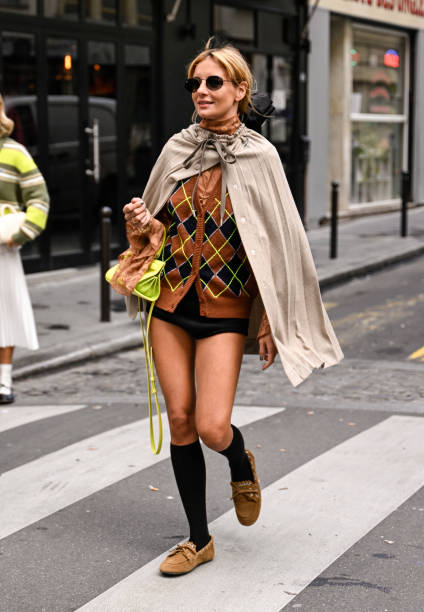 Guest is seen wearing a cape, brown and lime green cardigan, lime green bag, black socks and brown shoes outside the Lacoste show during Womenswear...