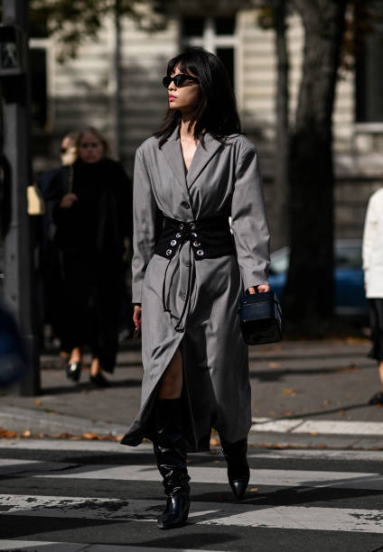 Guest is seen wearing a gray trench coat, black and silver belt, black boots and black sunglasses outside the Miu Miu show during the Womenswear...