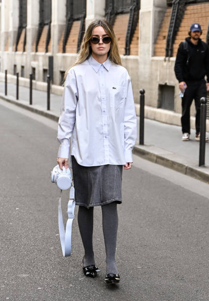 Guest is seen wearing a Lacoste button shirt, gray skirt, gray leggings, black shoes and white bag outside the Lacoste show during Womenswear...