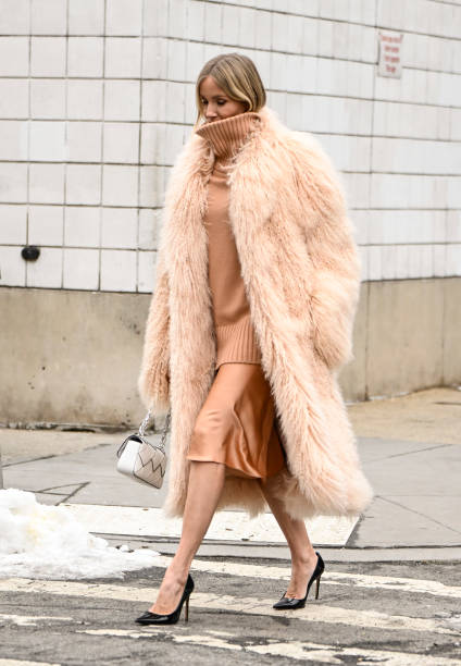 Guest is seen wearing a pink faux fur coat, pink sweater, silk skirt and black heels with white Michael Kors Collection bag outside the Michael Kors...