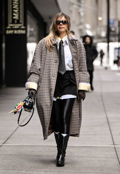 Guest is seen wearing a plaid coat, white shirt, gray tie, black shorts and black knee high boots with black sunglasses outside the Sandy Liang show...