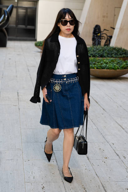 Guest is seen wearing a white shirt, black cardigan, blue denim skirt, black shoes, black sunglasses and carrying a black bag outside the Toteme show...