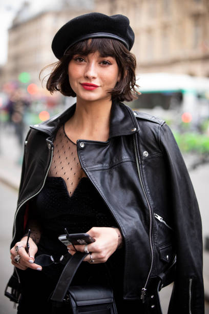 Guest, wearing a black mini dress, black leather jacket, black boots, black bag and hat, is seen outside Redemption on Day 4 Paris Fashion Week...
