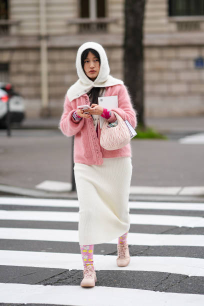 Guest wears a balaclava, a pink cardigan, a white skirt , floral print tights, sneakers shoes, outside Miu Miu , during the Womenswear Fall/Winter...