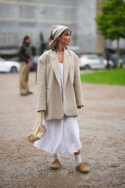Guest wears a beige silk scarf as a headband, a white long dress, a beige oversized blazer jacket, a beige and white latte striped print pattern...