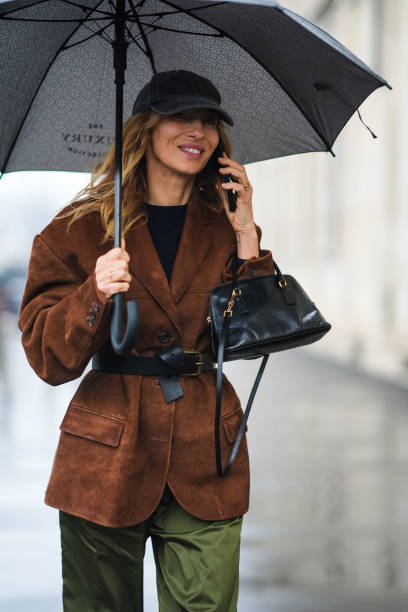 Guest wears a black cap hat, a black top, a brown suede oversized blazer jacket, a black leather bag , outside Prada, during the Milan Fashion Week -...