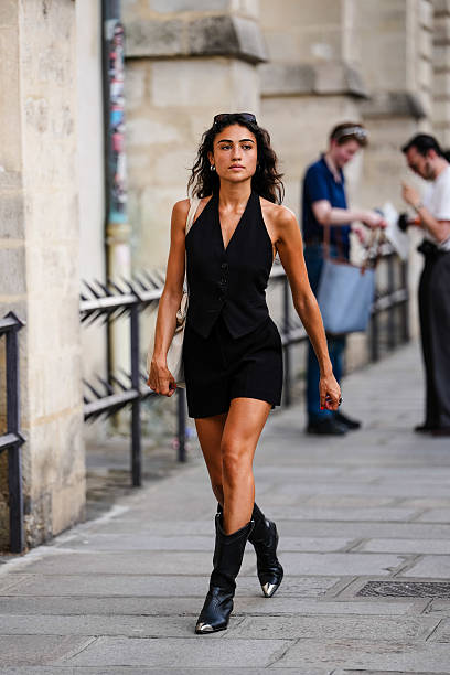 Guest wears a black halter-neck vest with button detailing, paired with matching black shorts. The ensemble is complemented by black cowboy boots...