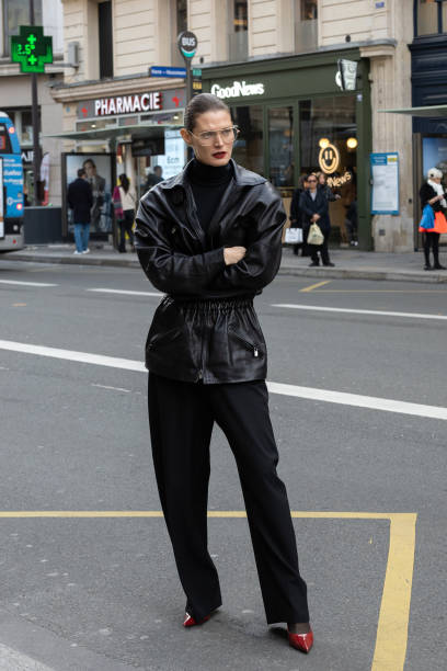 Guest wears a black leather jacket, black turtleneck, wide-leg black trousers, red pointed-toe heels, and clear-framed glasses outside Magda Butrym...