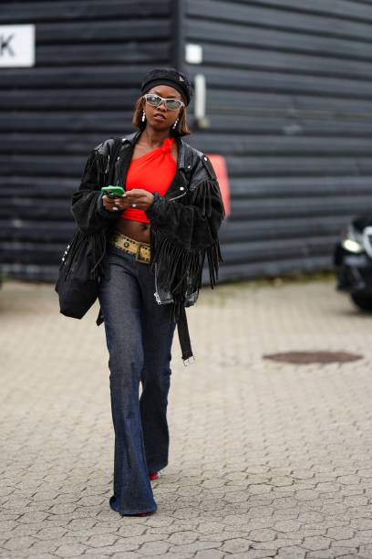 Guest wears a black nylon beret hat from Prada, silver sunglasses, silver earrings, a neon red shoulder-off / cropped top, a black shiny leather...