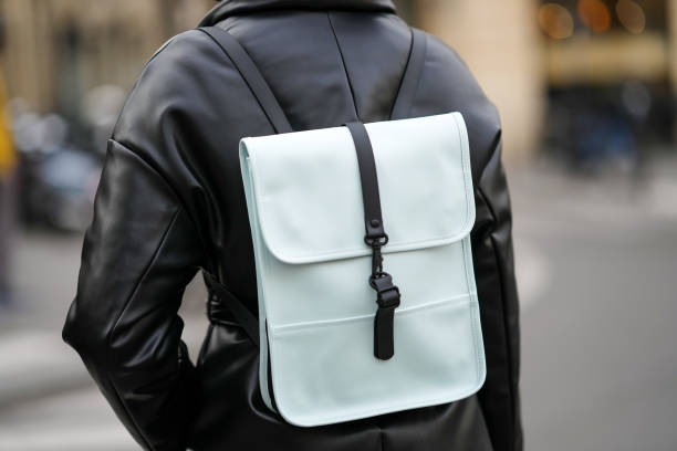 Guest wears a black shiny leather puffy / belted coat, a black and blue leather back pack bag, outside The Row, during Paris Fashion Week -...