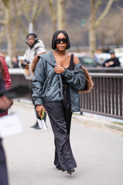 Guest wears a bomber jacket with brown fur, a black tank top, black wide-leg pants, black high heels, sunglasses, outside Chanel, during the...