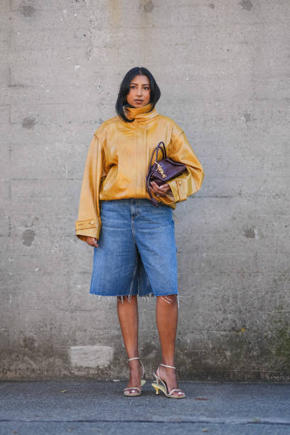 Guest wears a brown shiny leather jacket with puff sleeves, a burgundy leather bag, blue ripped denim / jeans shorts / jorts, kitten heels shoes,...