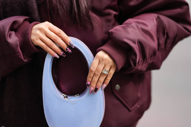 Guest wears a burgundy bordeaux oversized bomber jacket, shimmery light blue Coperni bag, colored nail polish, outside Altuzarra, during the New York...