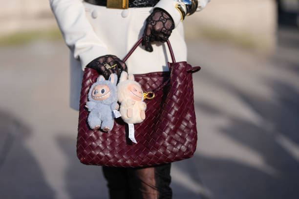 Guest wears a burgundy bordeaux woven Bottega Veneta Andiamo leather bag, light blue Labubu bag charm, cream Labubu bag charm, outside Elie Saab,...