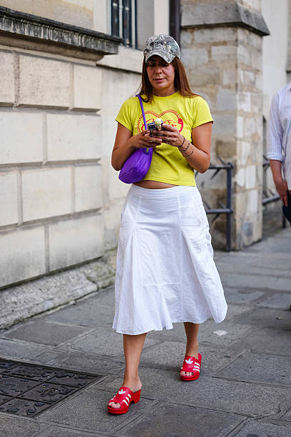 Guest wears a camouflage-patterned baseball cap and a bright yellow cropped T-shirt with a graphic print in red. A purple shoulder bag with a curved...