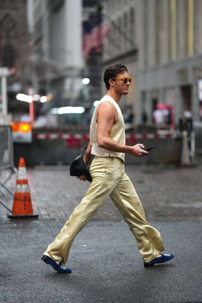 Guest wears a cream-color full look, a waist coat, flared lustrous pants, blue flat shoes, outside Alice & Olivia, during New York Fashion Week, on...