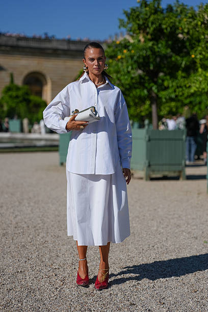 Guest wears a crisp white button-up shirt with a classic collar and long sleeves. The shirt is paired with a matching white midi skirt. Accessories...