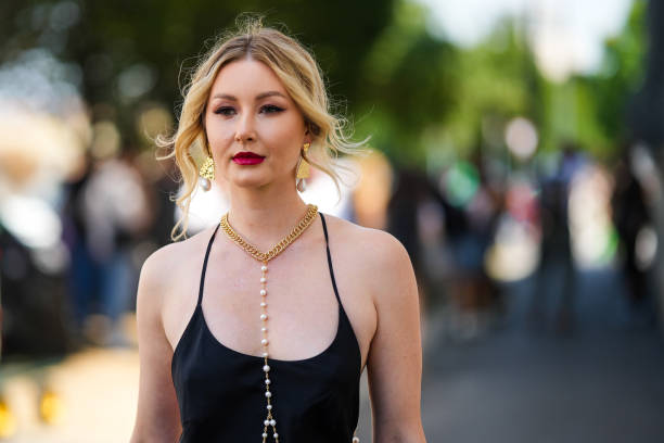Guest wears a gold with pearl pendant earrings, a gold necklace with long pearls pendant details, a black tank-top long summer dress, outside the...