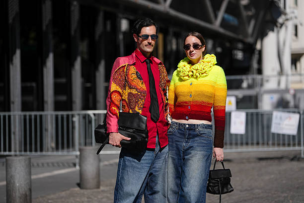 Guest wears a multicolored knitted cardigan with a gradient from yellow to red, featuring a textured ruffled collar. Paired with wide-leg blue denim...