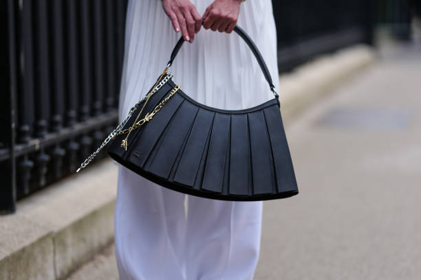 Guest wears a shiny black Lacoste leather bag, white outside Lacoste, during the Paris Fashion week Women's Fall/Winter 2025-2026 on March 9, 2025 in...